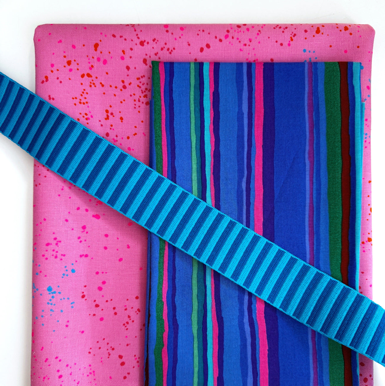 Pink speckled cotton fabric paired with blue striped fabric and teal striped webbing for sewing handmade bags, totes, and accessories.