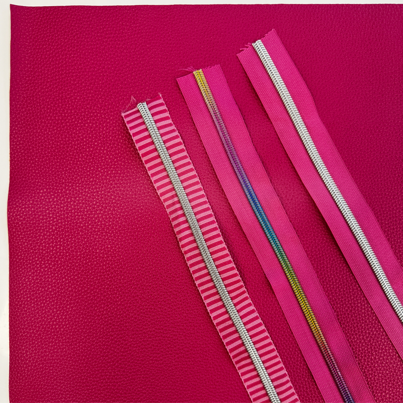 Pink zipper tapes with silver and rainbow zipper teeth displayed on coordinating pink vinyl for sewing handbags, wallets, pouches, and handmade accessories.