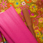A bright pink quilted chevron-patterned fabric or mat is draped over a colorful floral surface, with a rolled brown strap or band placed diagonally across the scene.