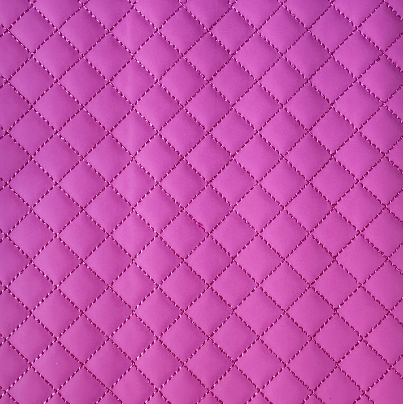 A close-up of a quilted fabric texture in a vibrant magenta pink, showing a repeating diamond pattern stitched together.