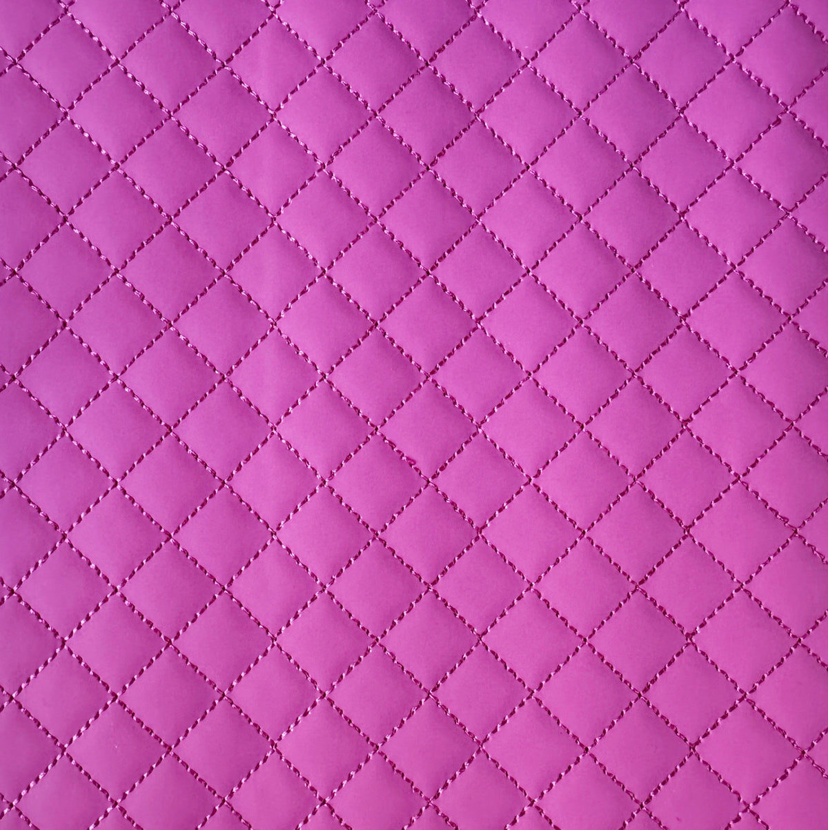 A close-up of a quilted fabric texture in a vibrant magenta pink, showing a repeating diamond pattern stitched together.