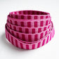 A coiled roll of woven strapping with alternating vertical stripes in bright pink and magenta tones, photographed on a clean white background.