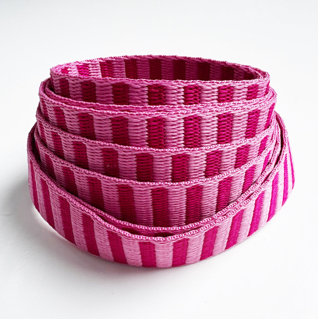 A coiled roll of woven strapping with alternating vertical stripes in bright pink and magenta tones, photographed on a clean white background.