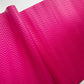 A close-up of a bright pink textured surface with a repeating chevron or zigzag embossed pattern, shown with a folded corner revealing a white background.