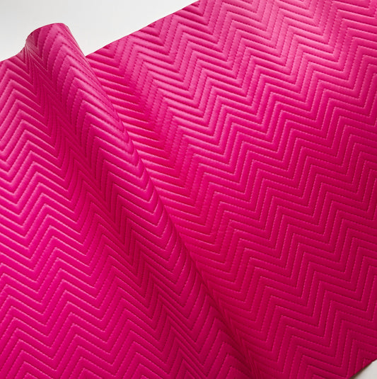 A close-up of a bright pink textured surface with a repeating chevron or zigzag embossed pattern, shown with a folded corner revealing a white background.