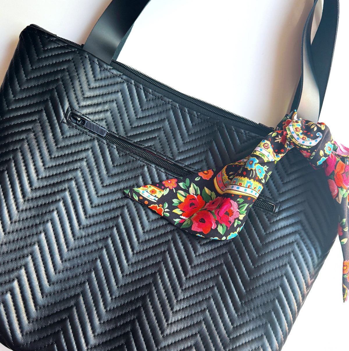 Black textured bag with colorful floral strap on a white background