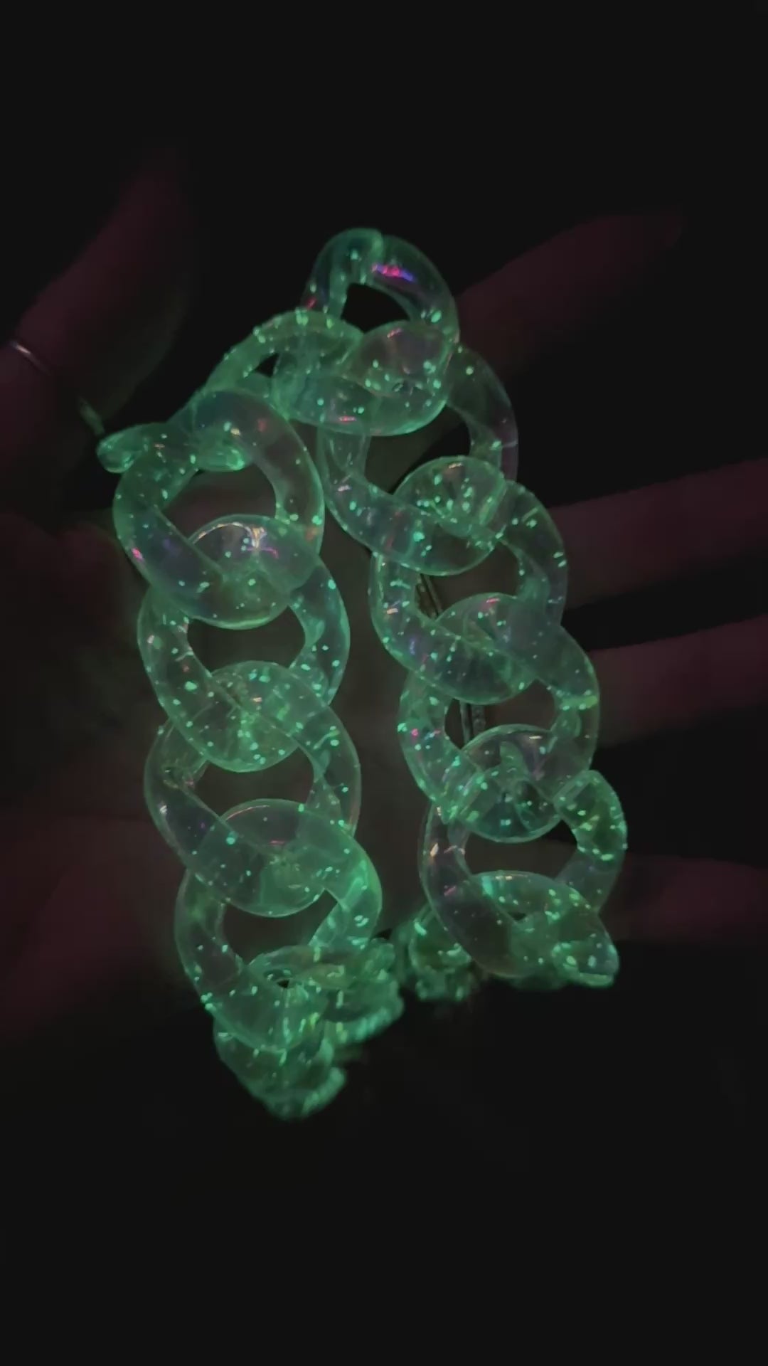 A video of a glow-in-the-dark neon green acrylic chunky chain strap held in hand.