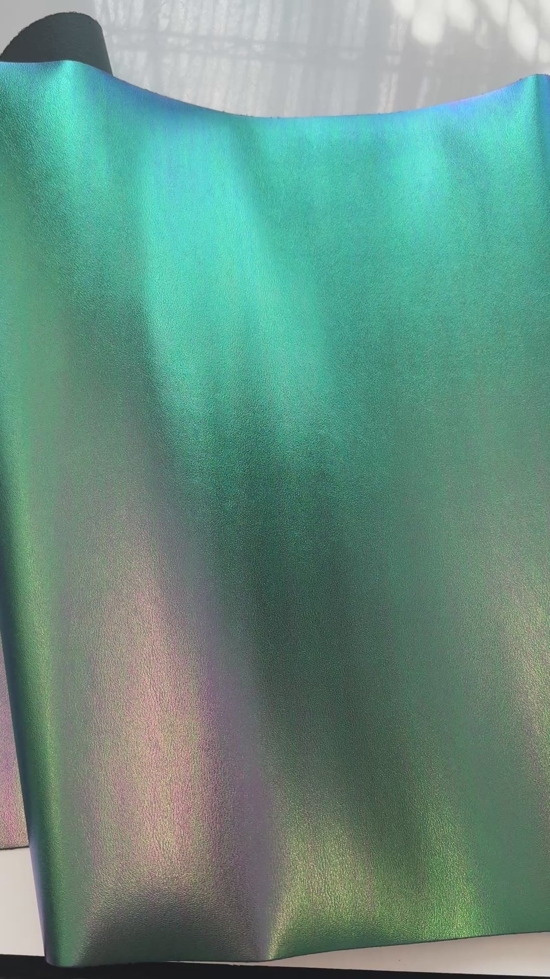 Video of high-quality iridescent green synthetic leather material with a smooth, reflective surface for bags