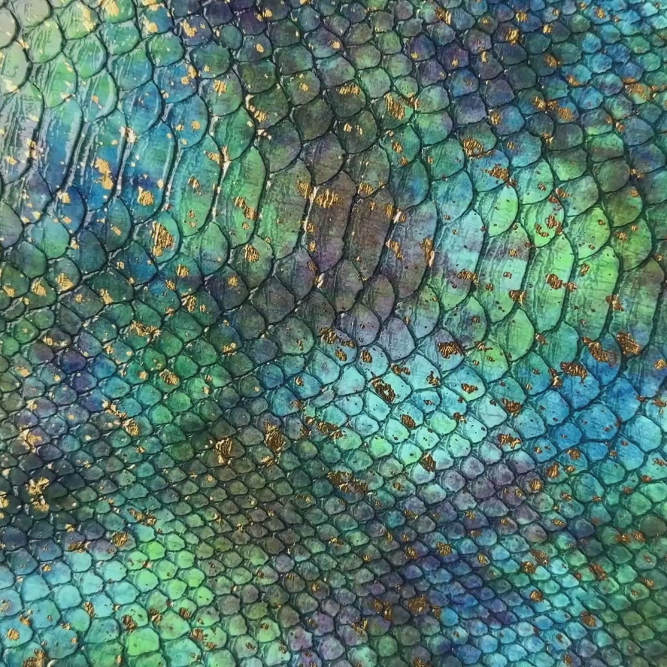 Close-up video of teal and blue embossed serpent vinyl with a scale texture and gold foil accents. 