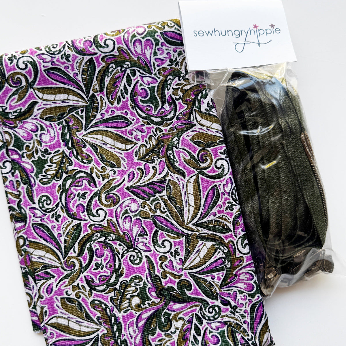 Sew Hungry Hippie bag-making supplies featuring vibrant purple cotton fabric with an abstract swirling pattern in dark olive green, white, and black, paired with dark olive green continuous zipper chain and matching metal zipper sliders. Coordinating fabric and zipper supplies for handmade handbags, zipper pouches, cosmetic bags, and DIY sewing projects.
