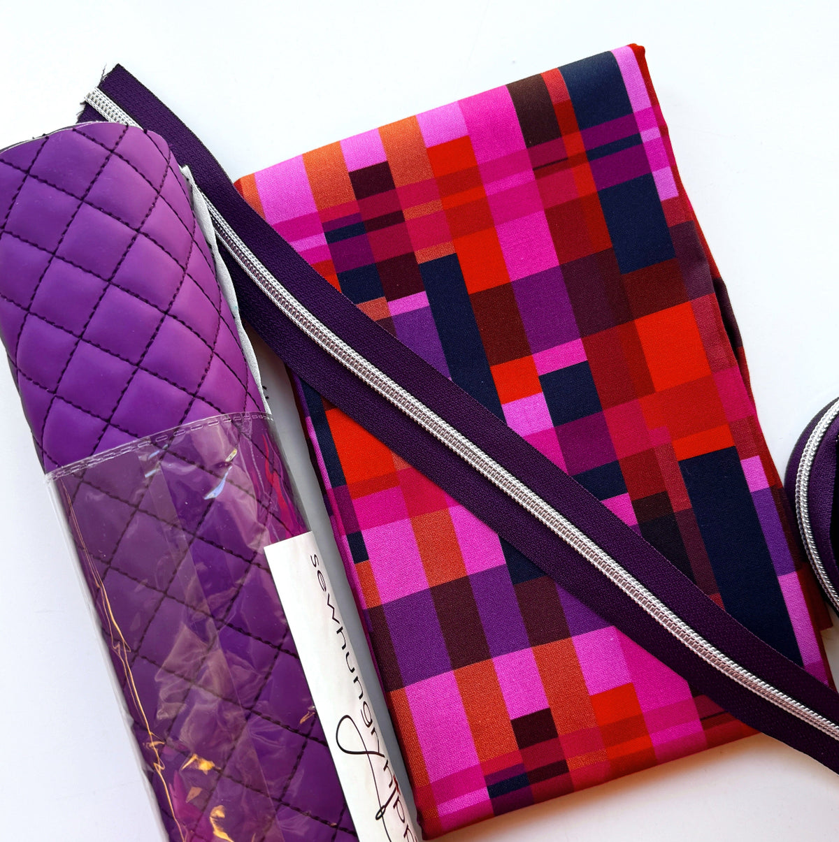 Purple bag-making supplies featuring diamond-quilted vinyl fabric, colorful pixelated geometric cotton fabric in magenta, red, dark purple, and navy blue, and matching dark purple continuous zipper tape with silver metal teeth. Coordinating materials for DIY handbags, quilted purses, and custom sewing projects.