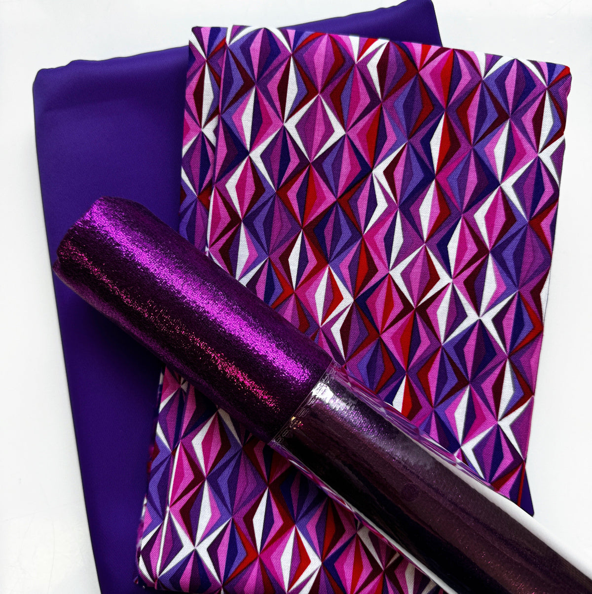 Purple bag-making materials featuring geometric patterned fabric, solid purple fabric, and glossy metallic pink vinyl
