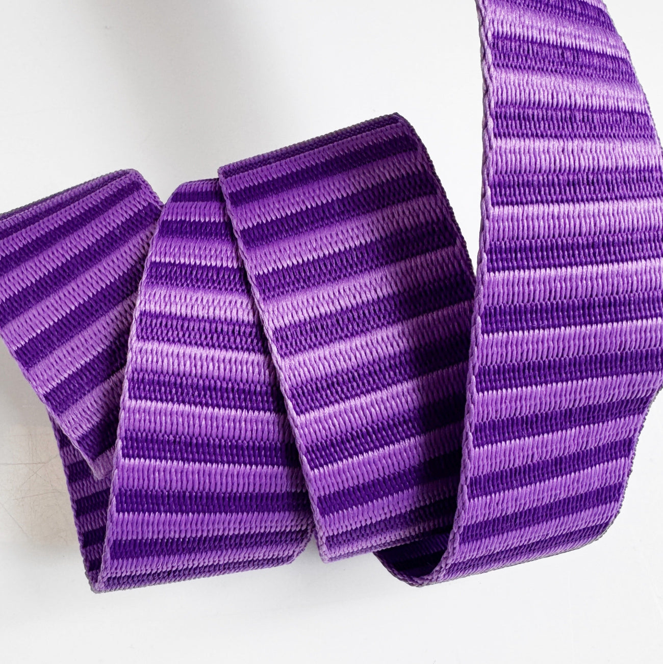 A 1.5-inch wide jacquard woven webbing strap featuring a monochromatic dark purple and medium purple horizontal stripe pattern, neatly coiled against a white background.