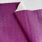 A close-up of a sheet of purple glitter wrapping paper with silver reflective speckles, showing a folded corner that reveals a white backing.