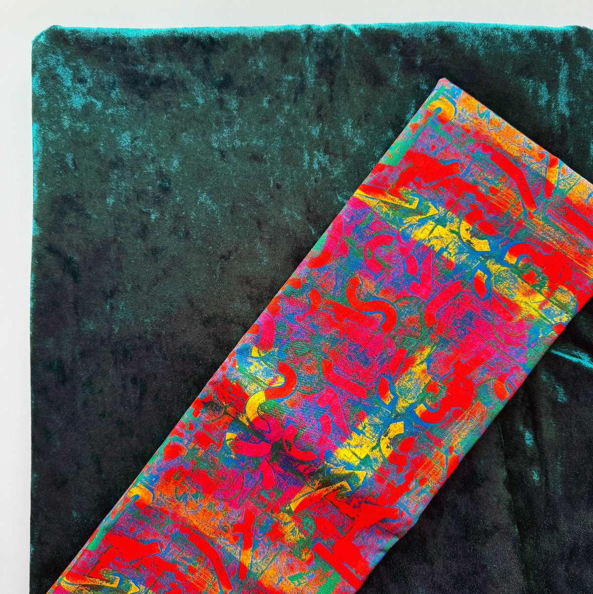 A close-up of a folded multicolor abstract-patterned fabric placed diagonally over a dark teal velvet background.