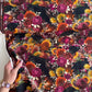 Hand holding a fabric "Ravenwood" fabric  showing the "Eerie" pattern dark, maximalist floral design with black crows, sunflowers, and vibrant roses.