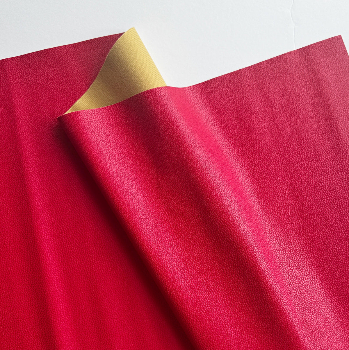  Close-up of vibrant fuchsia red leatherette vinyl fabric showing a detailed pebbled grain texture for making bags and wallets.