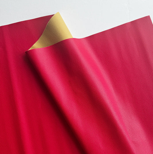  Close-up of vibrant fuchsia red leatherette vinyl fabric showing a detailed pebbled grain texture for making bags and wallets.