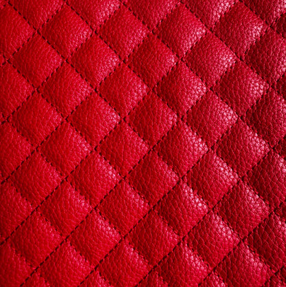 A close-up of bright red quilted leather texture with a repeating diamond pattern and pebbled grain.