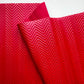 A close-up of a bright red textured fabric or material with a raised chevron pattern, folded over against a white background.
