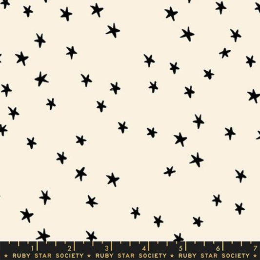 Cream-colored fabric with a scattered pattern of small, hand-drawn black stars, featuring a Ruby Star Society measuring ruler at the bottom edge.