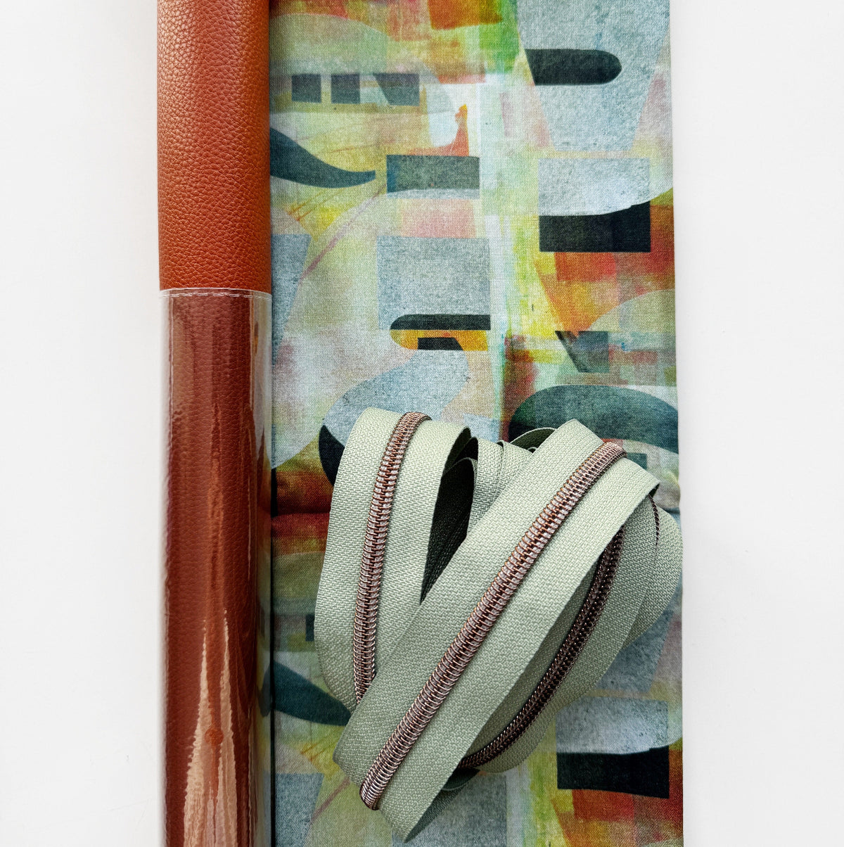 Sage green nylon zipper with copper coil, brown vinyl, and multicolor abstract fabric for bag making