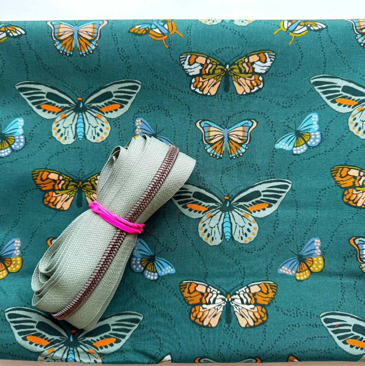 Sage green zipper tape on dark teal fabric with colorful illustrated butterfly print for bag making