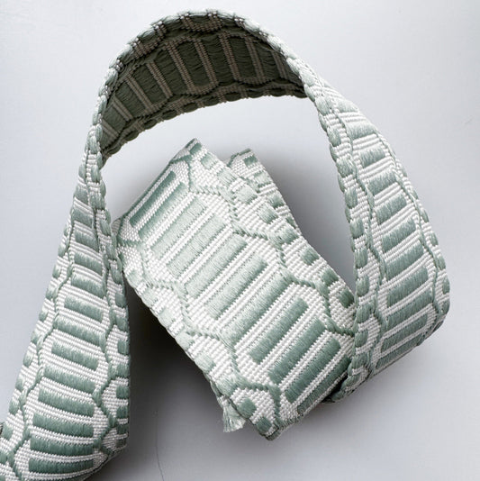 A light sage green and white woven fabric belt with a geometric pattern, folded and displayed on a light gray background.