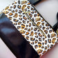 A close-up of a handbag featuring a white leopard print panel with black and brown spots, contrasted with a glossy black side panel and a gold-tone zipper.