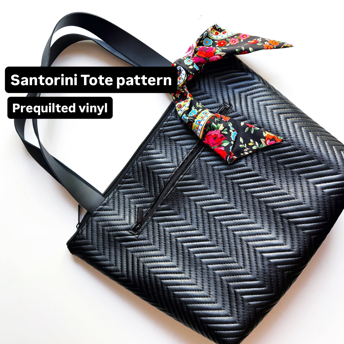Black herringbone patterned tote bag with a colorful floral ribbon on a white background