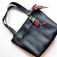 Black zigzag patterned bag with a colorful floral ribbon on a white background
