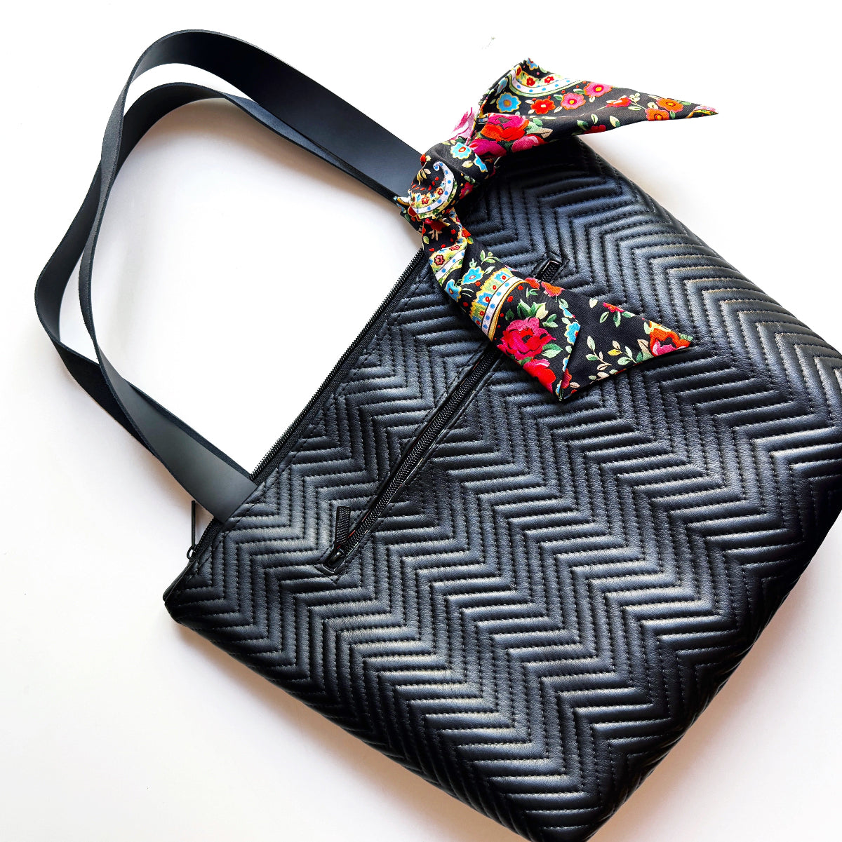 Black zigzag patterned bag with a colorful floral ribbon on a white background