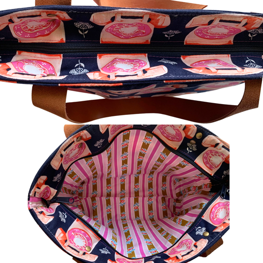 A tote bag shown from the front and back, featuring a navy blue exterior with a pink and orange retro rotary phone pattern, tan leather handles, and a pink striped interior.