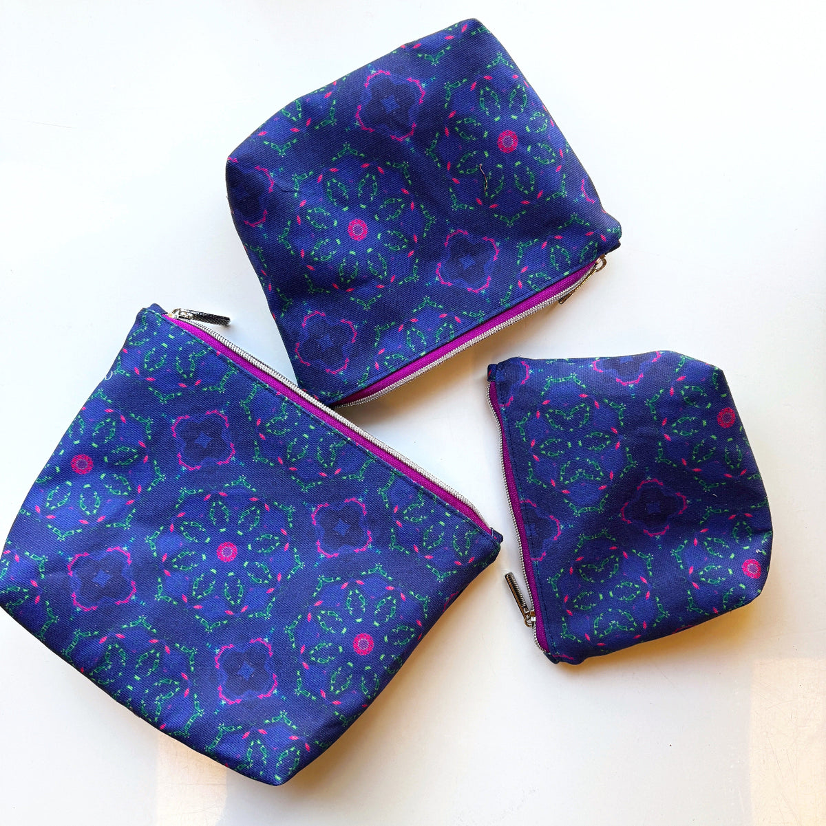 Set of three handmade zippered pouches featuring Sew Hungry Hippie Blue Kaleidoscope Cotton Canvas Fabric with a vibrant blue background and bright purple and green geometric mandala-style patterns. Colorful cotton canvas sewing projects ideal for handmade zipper bags, cosmetic pouches, travel organizers, and everyday accessories.
