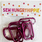 A packaged set of hot pink metal bag-making hardware by Sew Hungry Hippie inside a clear plastic bag with a flower-patterned cardboard header card.