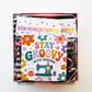 Sew Hungry Hippie bag-making hardware kit flat lay featuring snack pack zippers, magnets, black D-rings, silver metal D-rings and swivel clasps, and rolled zipper tape or straps in black, black-and-white stripes, and pink heart prints. Includes a clear plastic storage container, pink box, and colorful retro “Stay Groovy with Sewing” card decorated with 1970s-style flowers and a vintage sewing machine. Sewing supplies for handmade handbags, zipper pouches, purses, and DIY accessories.
