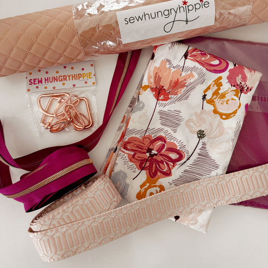 Sewing supplies featuring pink quilted fabric, floral fabric, burgundy zipper, rose gold bag hardware, and decorative webbing.