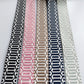 Five woven elastic straps with geometric patterns are arranged vertically side-by-side on a white background. The straps feature black and white, pink and white, tan and white, navy and white, and light gray and white patterns.