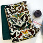 A fabric zippered pouch with a vintage-style butterfly print on a cream background, displayed next to a folded dark green fabric piece and a small packaged sewing thread spool with a tag reading 'SEW HUNGRIPHIDE'.