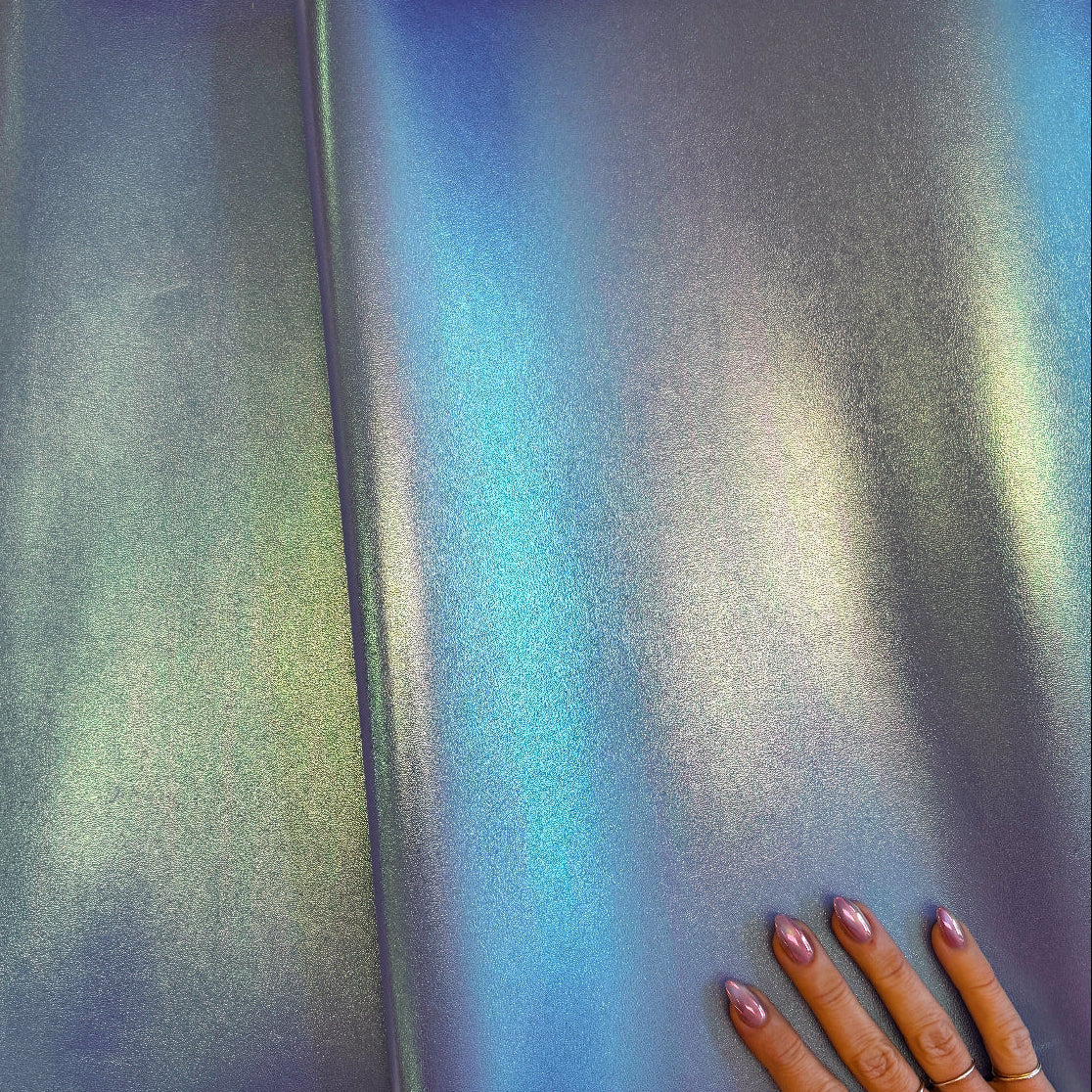 Gradient fabric swatch transitioning from blue to green with a hand for scale on a beige background