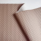 A close-up of a quilted fabric cushion cover in a dusty rose pink color, showing a diamond-stitched pattern and a folded corner revealing a white backing.