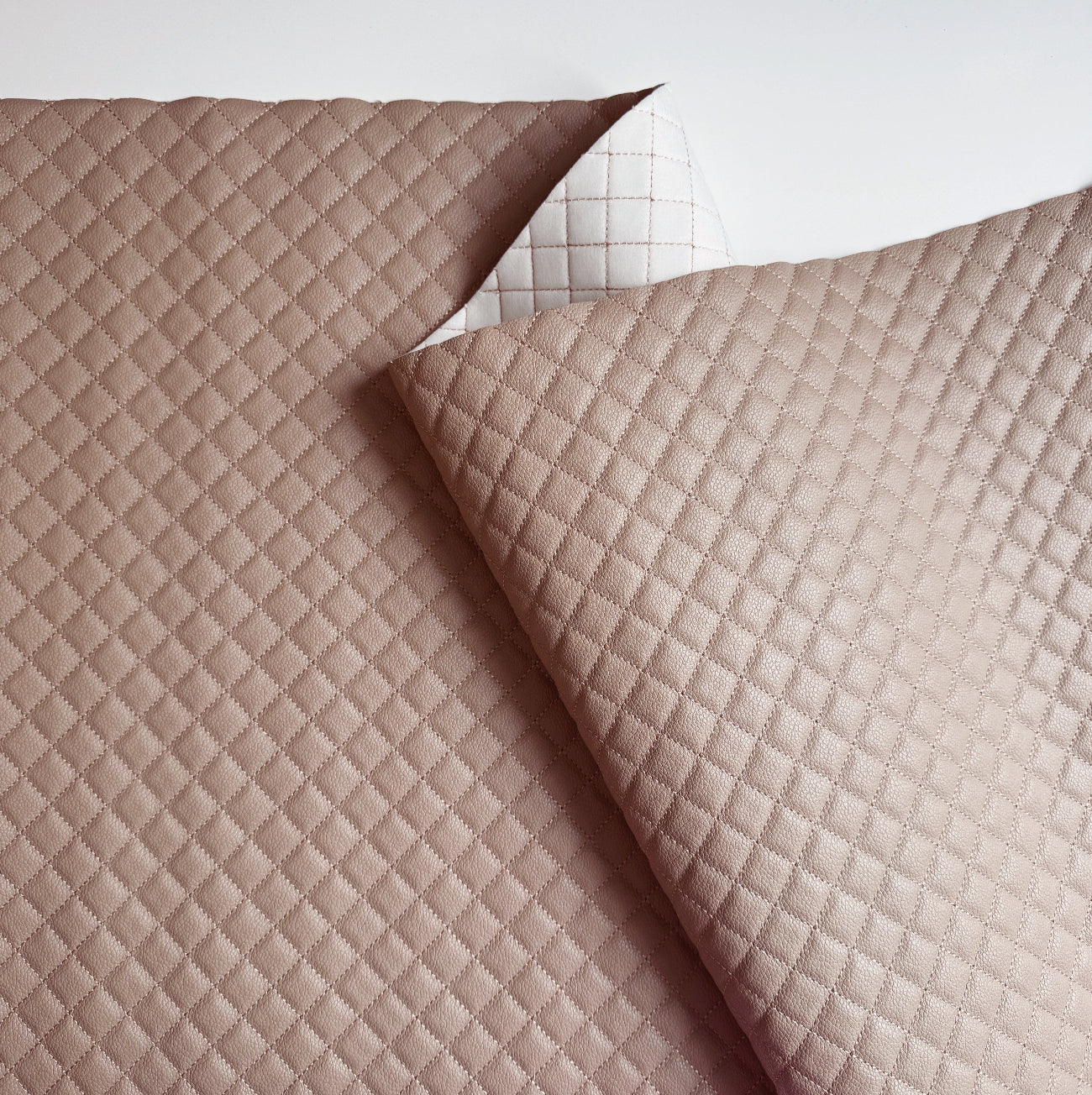 A close-up of a quilted fabric cushion cover in a dusty rose pink color, showing a diamond-stitched pattern and a folded corner revealing a white backing.