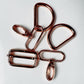 Five metallic rose gold hardware clips and rings arranged on a plain white background.