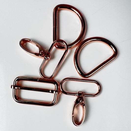 Five metallic rose gold hardware clips and rings arranged on a plain white background.