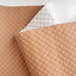 A folded piece of beige-colored vinyl fabric featuring a quilted diamond pattern with visible stitching, showing both the finished surface and the white backing.