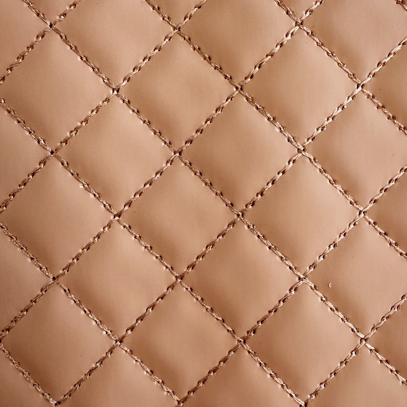 a detailed close-up of beige-colored vinyl with a quilted diamond stitch pattern, highlighting the texture and thread detail of the stitching.
