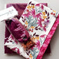 White floral cotton fabric featuring pink flowers, burgundy leaves, and mustard accents, paired with burgundy nylon bag lining and a burgundy zipper with rose-gold hardware.