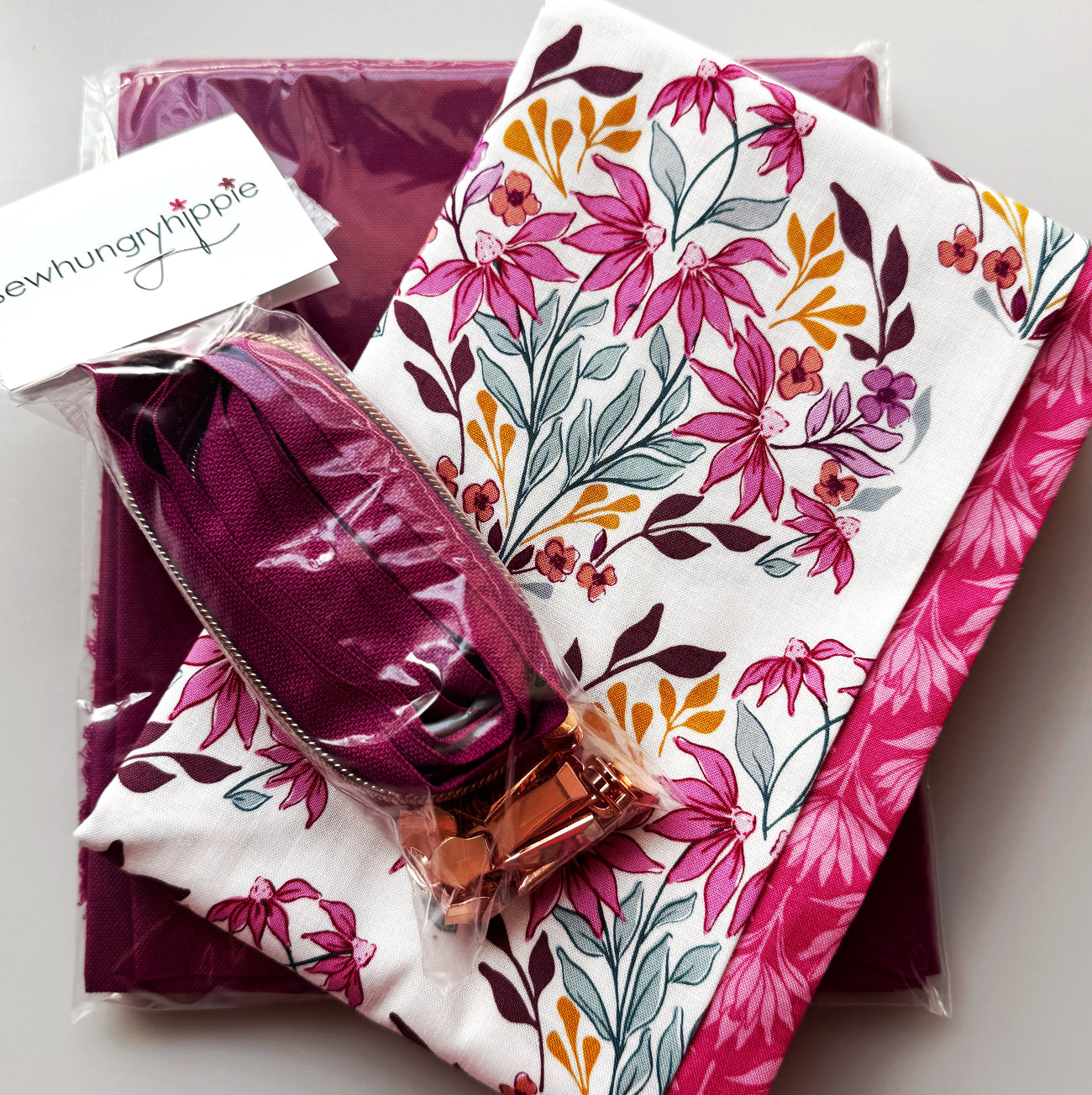 White floral cotton fabric featuring pink flowers, burgundy leaves, and mustard accents, paired with burgundy nylon bag lining and a burgundy zipper with rose-gold hardware.