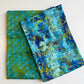 Two folded yards of SewHungryHippie MATCHUP 9 fabric coordinates. The bottom fabric features an abstract green-and-teal bubble pattern, while the top fabric displays a vibrant, textured abstract design in shades of blue, teal, purple, and lime green.