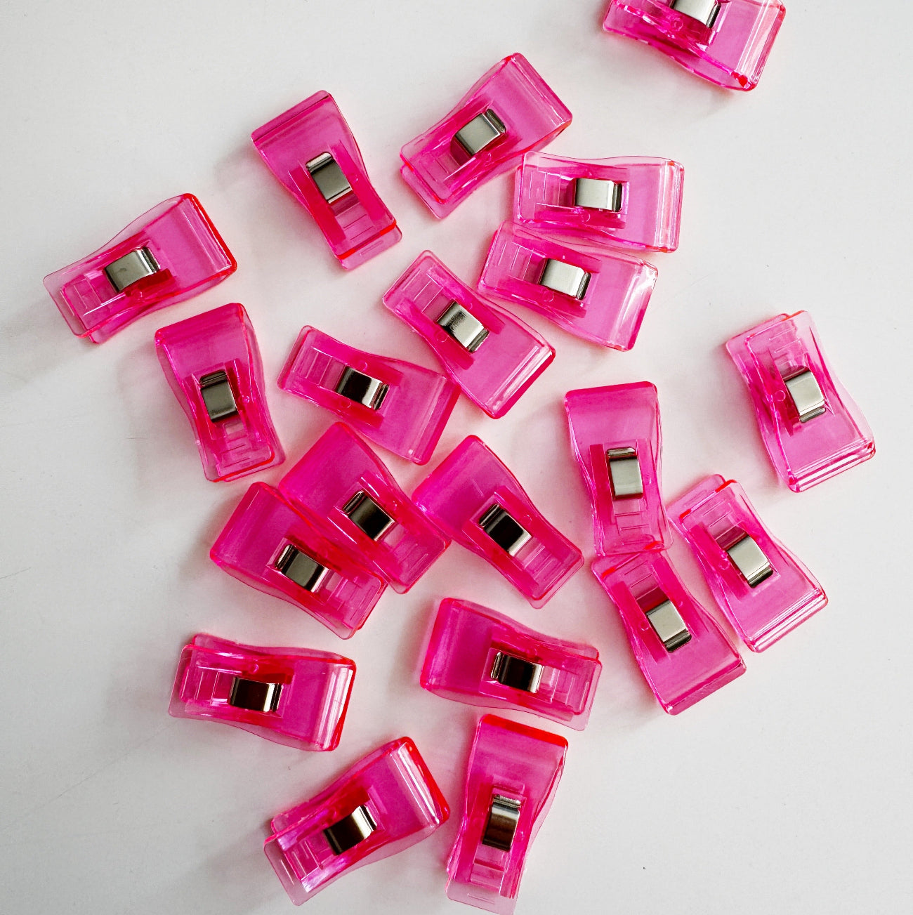 20 packs of translucent bright pink plastic sewing clips scattered on a white surface, commonly used for bag making and quilting.